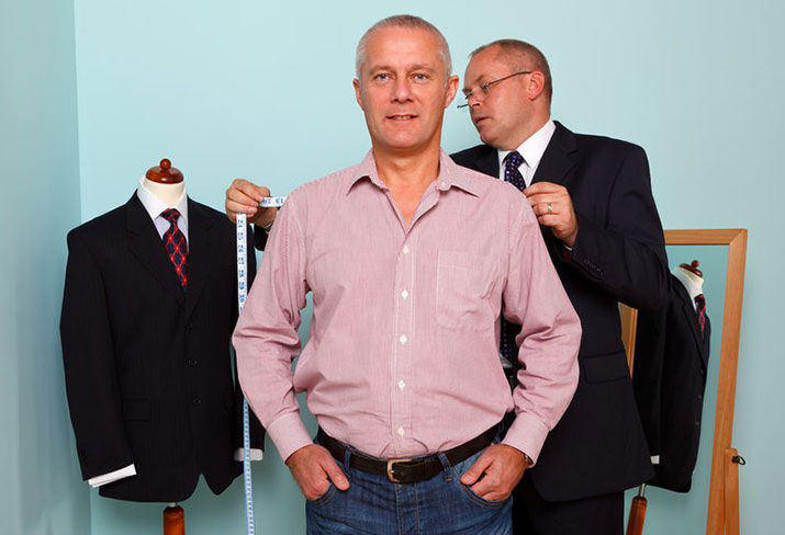 A tailor measuring the shoulder width of a man for the fitting of a new bespoke suit